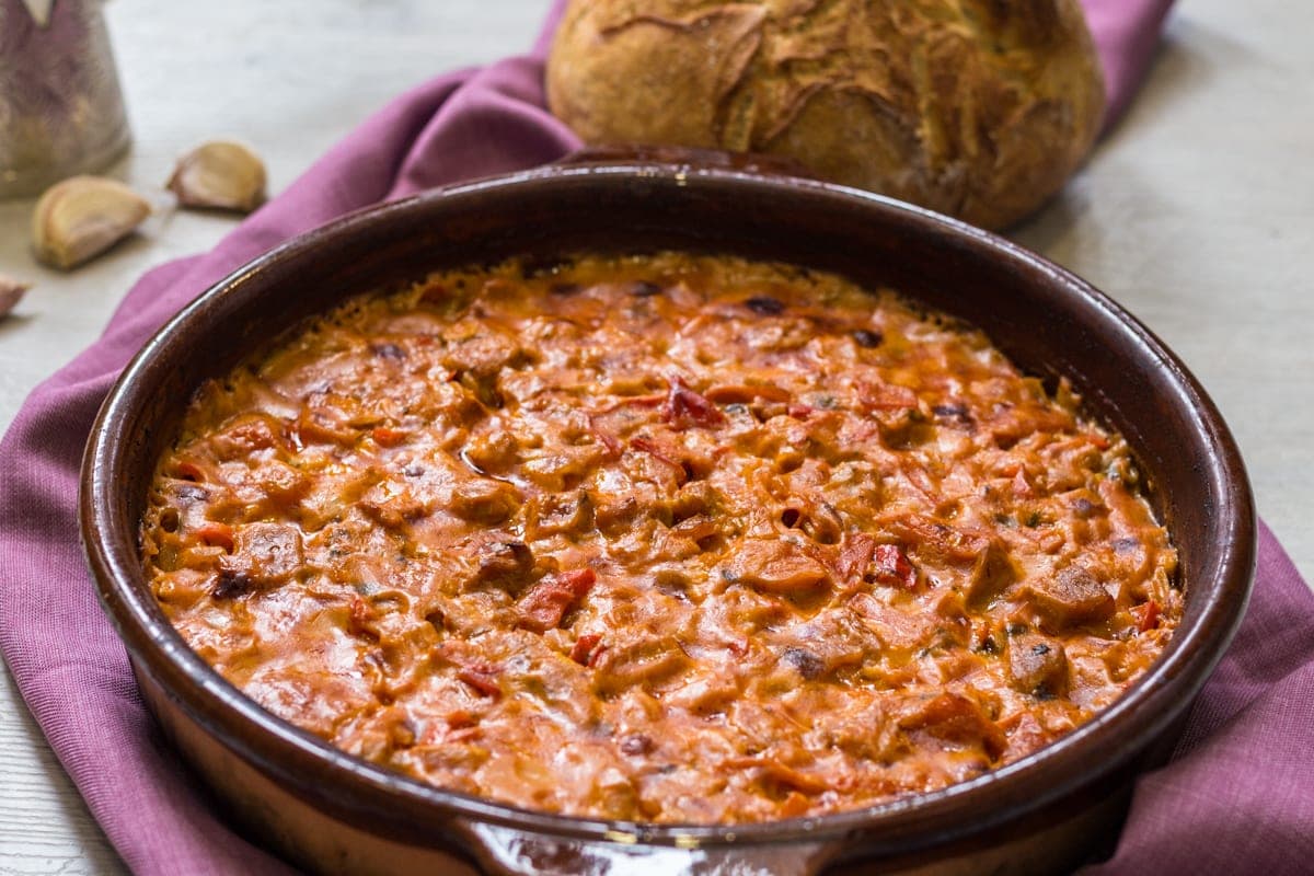 Fërgesë in a clay dish: peppers, tomatoes and melted gjizë cheese with pieces of meat