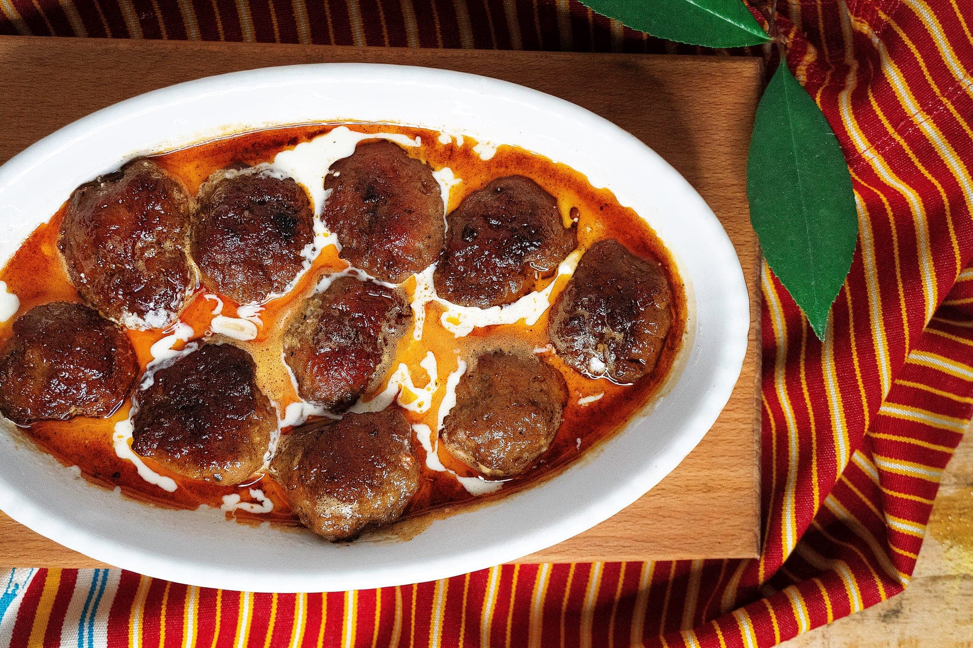 Browned Albanian qofte meatballs in an oval dish with tomato sauce and yogurt
