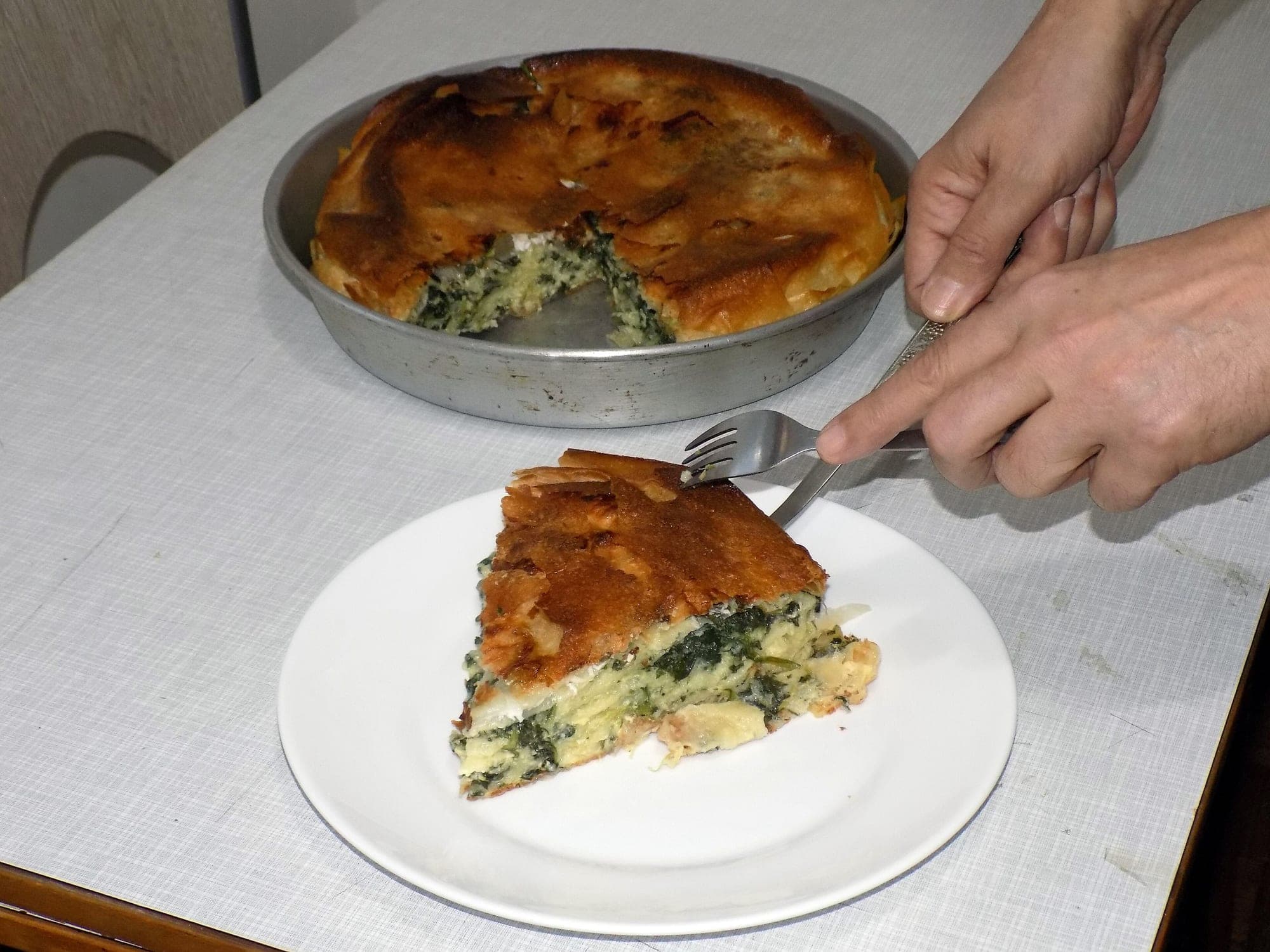 A slice of spinach and cheese byrek being served from the baking pan onto a white plate