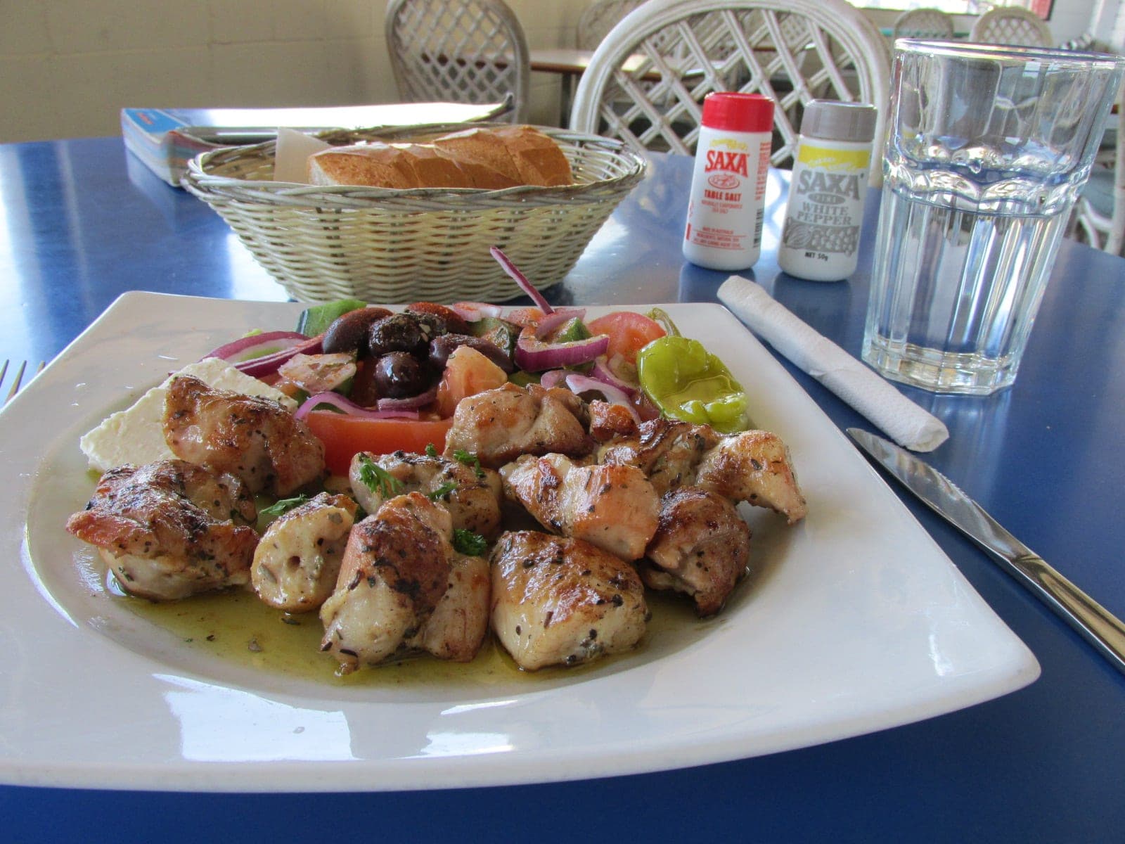 Plate of lemon and oregano chicken pieces with salad, olives and a pepper