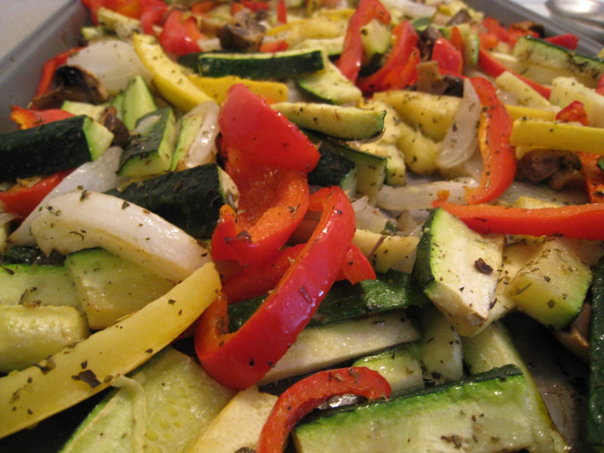 Roasted zucchini, yellow squash and red and yellow bell peppers on a baking tray